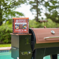 Box of Smokin' Pecan shell pellets on a grill with a blurred green outdoor background