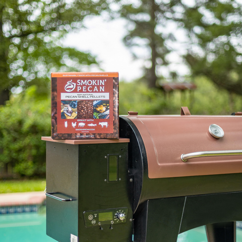 Box of Smokin' Pecan shell pellets on a grill with a blurred green outdoor background