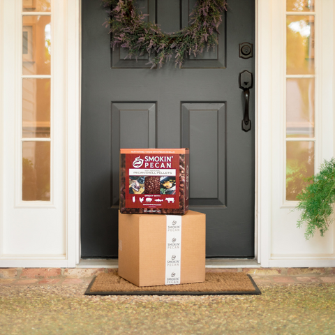 Cardboard box with a Smokin' Pecan product on a doormat in front of a house.