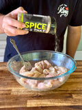 Person seasoning chicken in a glass bowl with 'SPICE THAT' container.