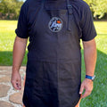 Person wearing a black apron with a logo outdoors on a grassy area