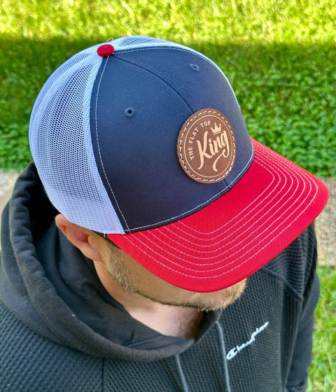 Person wearing a blue and red cap with a leather patch against a grassy background