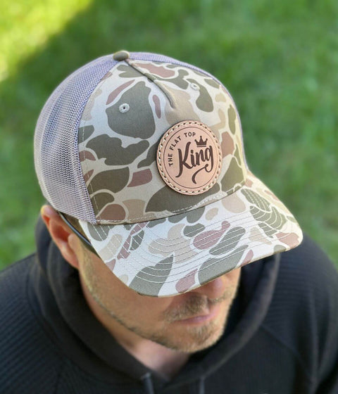 Camouflage trucker hat with leather patch on a person against a grassy background