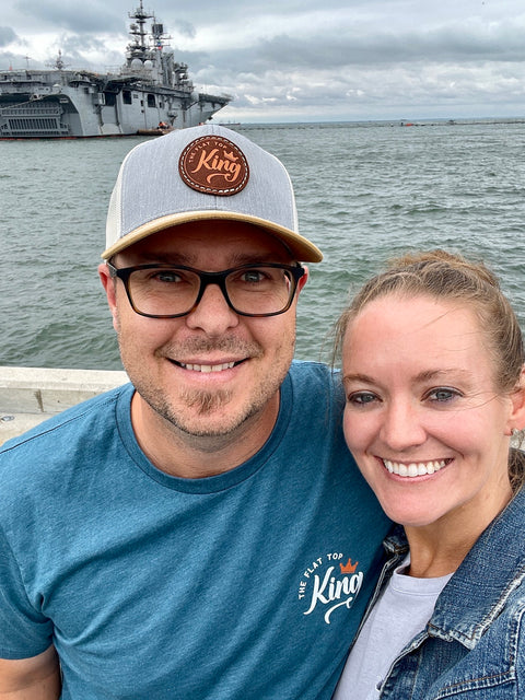 Two people posing for a selfie with a large ship in the background.